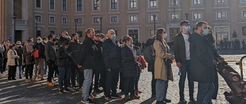 Menschen warten auf Einlaß auf den Petersplatz. Auf dem Platz gilt seit gestern Maskenpflicht, außerhalb auf italienischem Staatsgebiet nicht (bzw. ist Interpretationssache).