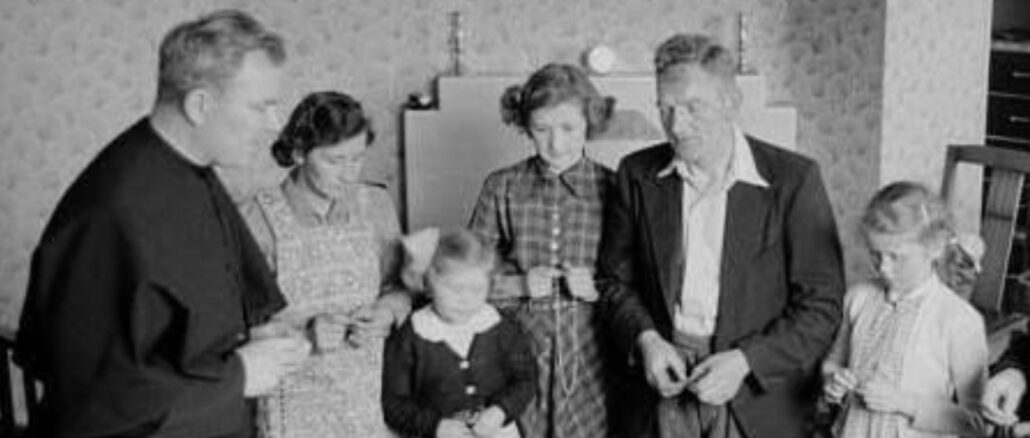 Priester betet zusammen mit einer Familie den Rosenkranz
